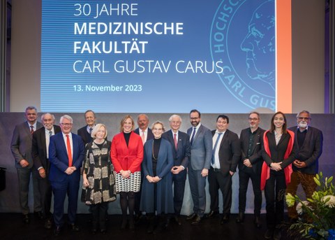 Eine Bühne mit vielen Menschen vor einem Banner "30 Jahre Medizinische Fakultät Carl Gustav Carus"