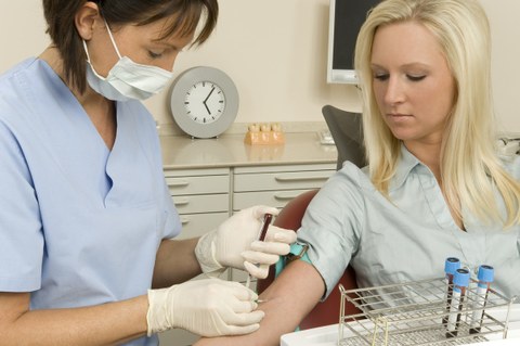 Eine medizinische Angestellte nimmt einer Frau Blut aus der Armbeuge ab.
