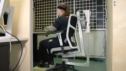 Fotoaufnahme einer Frau, die mit Sensoren ausgestattet auf einem Bürostuhl sitzt.