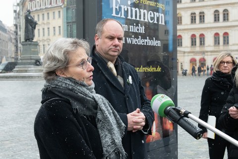 Prof. Staudinger und OB Hilbert stehen vor einem Plakat zum 13.2. auf dem Neumarkt und sprechen in ein Mikro