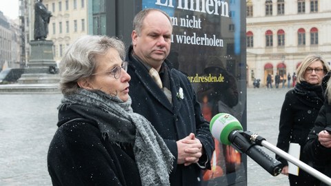 Prof. Staudinger und OB Hilbert stehen vor einem Plakat zum 13.2. auf dem Neumarkt und sprechen in ein Mikro