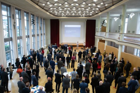 Blick in einen großen Saal mit vielen Menschen an Stehtischen.