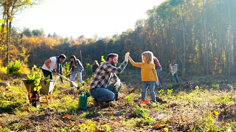 Ein hockender Mann und ein kleines Kind schlagen die Hände gegeneinander. Im Hintergrund forsten mehrere Menschen einen Wald auf.