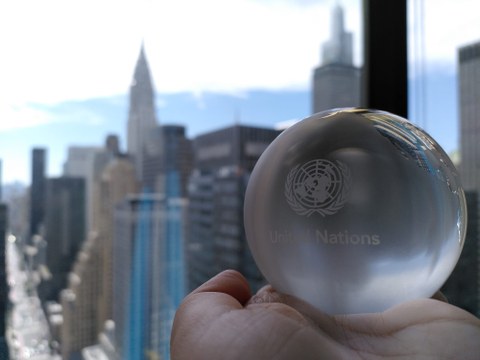 Eine Glaskugel, die die Erde symbolisiert, wird vor die Skyline von News York gehalten.