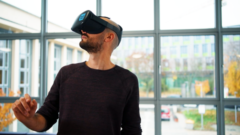 Photo of a man standing in front of a window and wearing a VR headset.