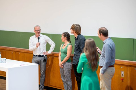 Prof. Hyman mit anderen Personen auf dem Podium mit einem Mikrofon in der Hand