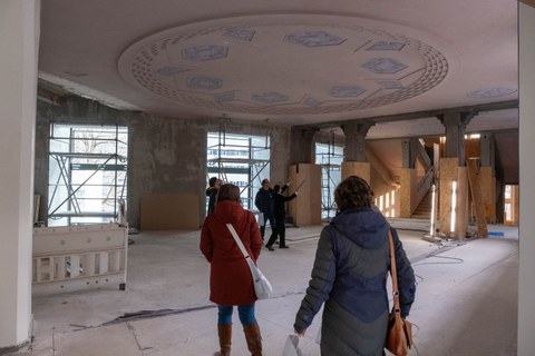 Mehrere Personen sehen sich auf einer Baustelle in einem Gebäude eine runde Deckenverzierung an.