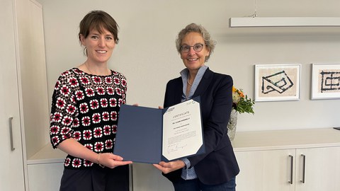 Foto von zwei Frauen bei der Übergabe einer Ernennungsurkunde in einem Büroraum.