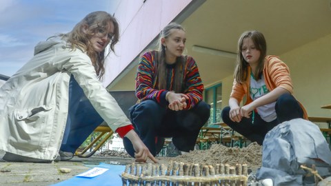 Drei junge Frau hocken auf dem Boden und bauen aus Sandund Holz eine Küstenlandschaft nach