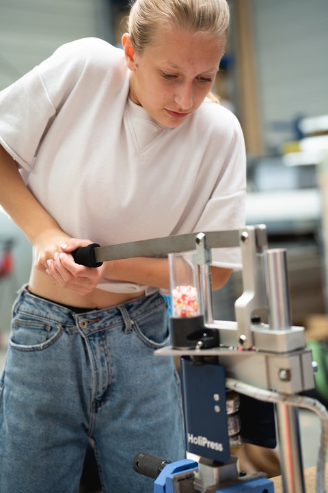 Foto einer jungen Frau, die an einer Maschine steht und einen daran befestigten Hebel bedient.