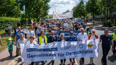 Fotoaufnahme eines Demonstrationszuges. In der ersten Reihe tragen Menschen ein Banner dem "Gemeinsam für Demokratie" steht.