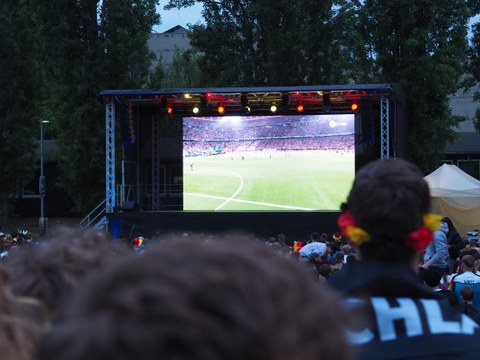 Fotoaufnahme von Menschen, die auf eine Leinwand schauen, auf der ein Fußballspiel gezeigt wird.
