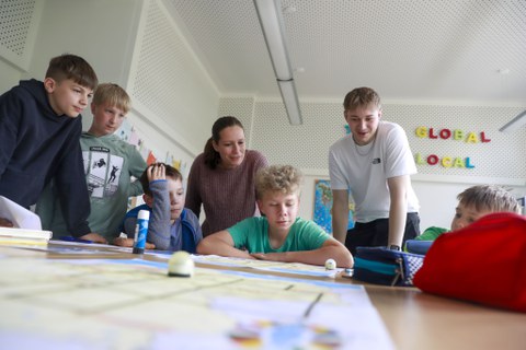 Fünf Kinder und zwei Studierende schauen gemeinsam auf eine Projektarbeit