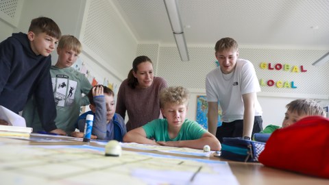 Fünf Kinder und zwei Studierende schauen gemeinsam auf eine Projektarbeit