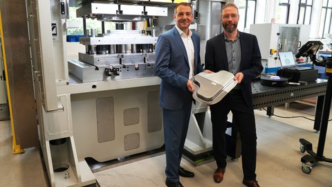 Prof. Andrés Lasagni und Prof. Alexander Brosius stehen vor einen technischen Anlage. Sie halten ein recyceltes Metallteil in den Händen.