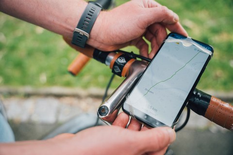 Fotoaufnahme eines Smartphones, das am Lenker eines Fahrrads angebracht ist und dessen Display eine Route in Dresden anzeigt.