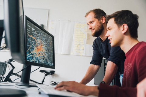 Fotoaufnahme von zwei Männern, die auf einen Computer-Bildschirm schauen. Dieser zeigt eine Karte von Dresden, auf der Fahrradrouten farbig markiert sind.