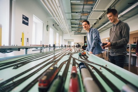 Fotoaufnahme von zwei jungen Männern, die im Eisenbahnbetriebslabor der TU Dresden stehen.
