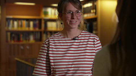 Fotoaufnahme der Philosophin Lisa Hecht, die in einer Bibliothek in einem Gespräch mit einer anderen Person ist.