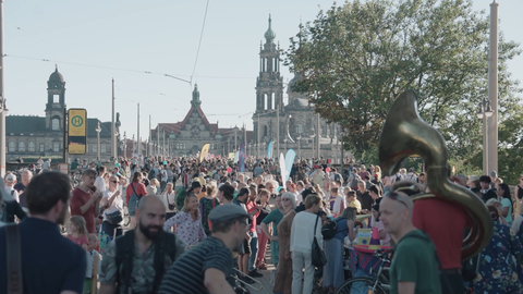 Fotoaufnahme einer Festmeile, die sich über die Dresdner Augustusbrücke erstreckt und voll mit Menschen ist. Im Hintergrund sind Gebäude der Dresdner Altstadt abgebildet.