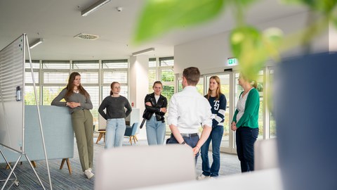 Fotoaufnahme von sechs Personen, die in einem großzügigen Büro stehen und einander zugewandt sind.