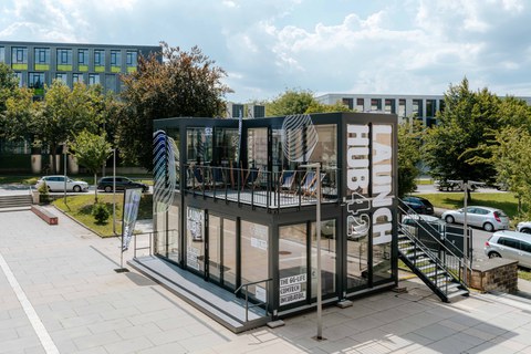 Fotoaufnahme eines Container-Gebäudes mit großflächigen Glasfassaden auf dem Platz vor dem Barkhausen-Bau der TU Dresden.