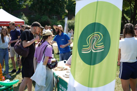 Menschen stehen an einem Infostand. Im Vordergrund ist eine Fahne mit dem Logo der TU-Umweltinitiative tuuwi