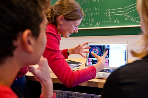 Zwei Schülern wird am Computer von einer Wissenschaftlerin ein physikalischer Prozess erklärt.
