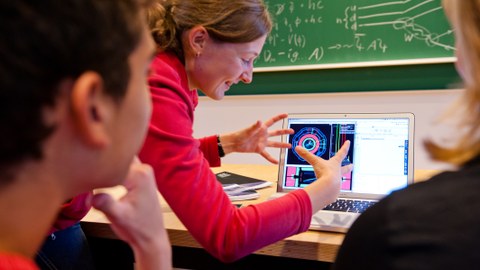 Zwei Schülern wird am Computer von einer Wissenschaftlerin ein physikalischer Prozess erklärt.