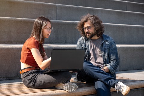 Bild zweier Studenten, die am Fritz-Foerster-Bau auf der Treppe sitzen und zusammen am Laptop arbeiten.