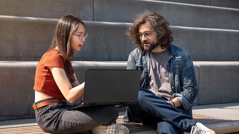 Bild zweier Studenten, die am Fritz-Foerster-Bau auf der Treppe sitzen und zusammen am Laptop arbeiten.