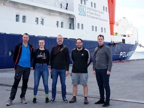 Gruppe von 5 Menschen vor einem Schiff.