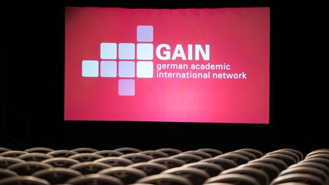 Fotoaufnahme eines projeziierten Bildes, das die GAIN-Konferenz ankündigt.