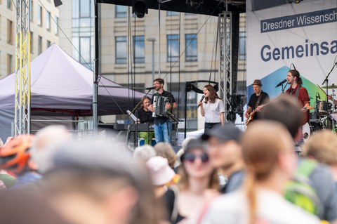 Foto der Dresdner Sinfoniker, die auf einer Bühne Musik machen. Im Vordergrund sind unscharf Köpfe von Besucherinnen und Besuchern abgebildet.