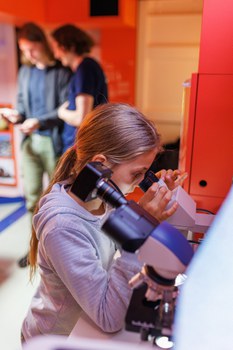 Foto von einem Mädchen, das in ein Mikroskop schaut.