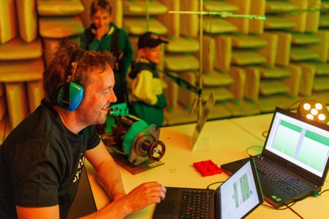 Foto von einem Mann, der an einem Laptop sitzt und Kopfhörer trägt.