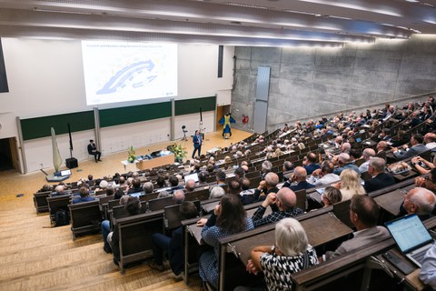 Foto aus einem Hörsaal der TU Dresden. Eine Person trägt vor. Die Sitzreihen sind gut gefüllt mit Personen.