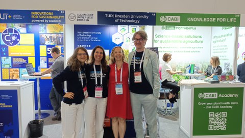Fotoaufnahme von drei TUD-Mitarbeitenden und einer weiteren Frau vor dem Messestand der TUD beim GSDC.