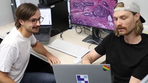 Foto von Marco Gustav, Erstautor der Veröffentlichung und Wissenschaftlicher Mitarbeiter am EKFZ für Digitale Gesundheit, und Dr. Nic G. Reitsam, Co-Autor und Pathologe an der Medizinischen Fakultät der Universität Augsburg. Beide besprechen die Daten der Studie.