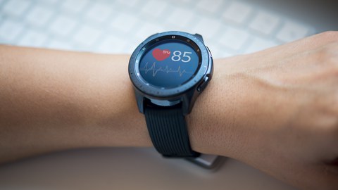 Fotoaufnahme eines Handgelenks, an dem sich eine Smartwatch befindet. Das Display zeigt einen Graphen zu den Herzschlägen sowie eine aktuelle BPM-Zahl.