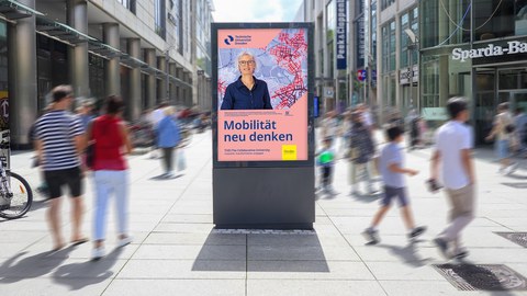 Das Foto zeigt einen Schaukasten mit einem Plakat der TU Dresden in einer belebten Einkaufsstraße.