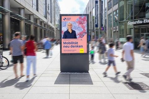 Das Foto zeigt einen Schaukasten mit einem Plakat der TU Dresden in einer belebten Einkaufsstraße.