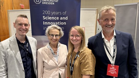 Jeremiah Peterson vom Alumni-Büro der TUD, Rektorin Prof. Ursula Staudinger, Alumni-Botschafterin Romy Frank und Peter Rosenbaum vom International Office stehen vor einem Banner der TU Dresden.