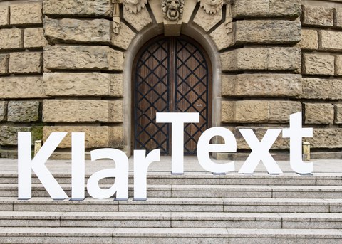 Foto von großen, weißen Buchstaben, die das Wort "KlarText" bilden auf einer Treppe vor einem Gebäude.