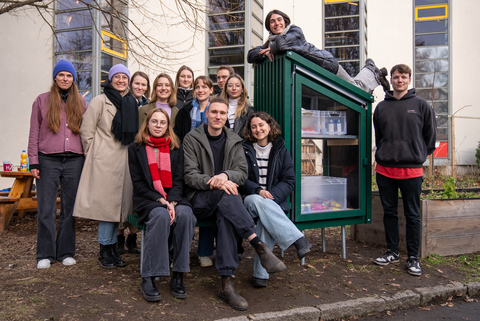 Foto: Eine große Gruppe von Menschen steht vor einer grünen Holzkonstruktion – den "Fairteilern".