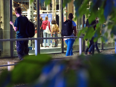 Foto eines TUD-Gebäudes, durch dessen Glasfassade eine kleine Menschengruppe erkennbar ist.