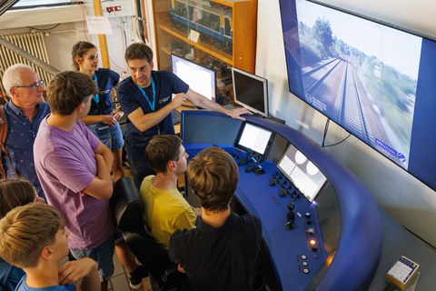Foto vom Eisenbahnsimulator der TU Dresden, an dem sich eine kleine Menschengruppe befindet.