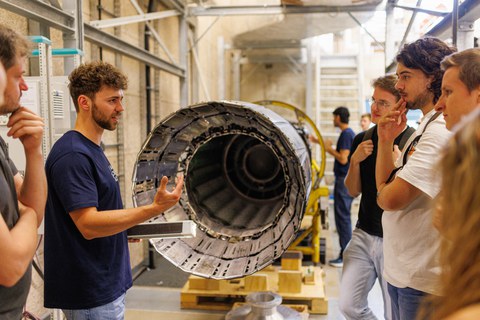 Foto einer metallenen Röhre, an der Menschen stehen, die ein Gespräch führen.