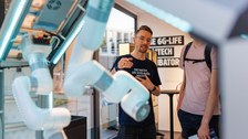 Foto von zwei Personen, die an einem Roboter-Demonstrator stehen und sich unterhalten.