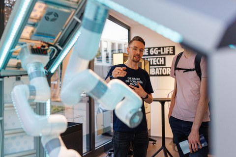 Foto von zwei Personen, die an einem Roboter-Demonstrator stehen und sich unterhalten.